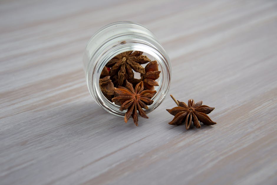 Close-up of star anise spices spilling from a glass jar on a wooden surface.